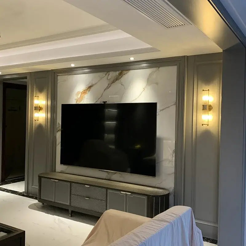A sleek modern flat-screen television with black bezel mounted on marble wall near chrome glass rod wall sconce vanity lights