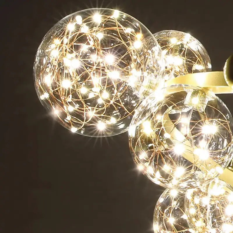Modern chrome and gold Decorbites crystal chandelier with golden filament string lights in clear glass spheres glowing warmly