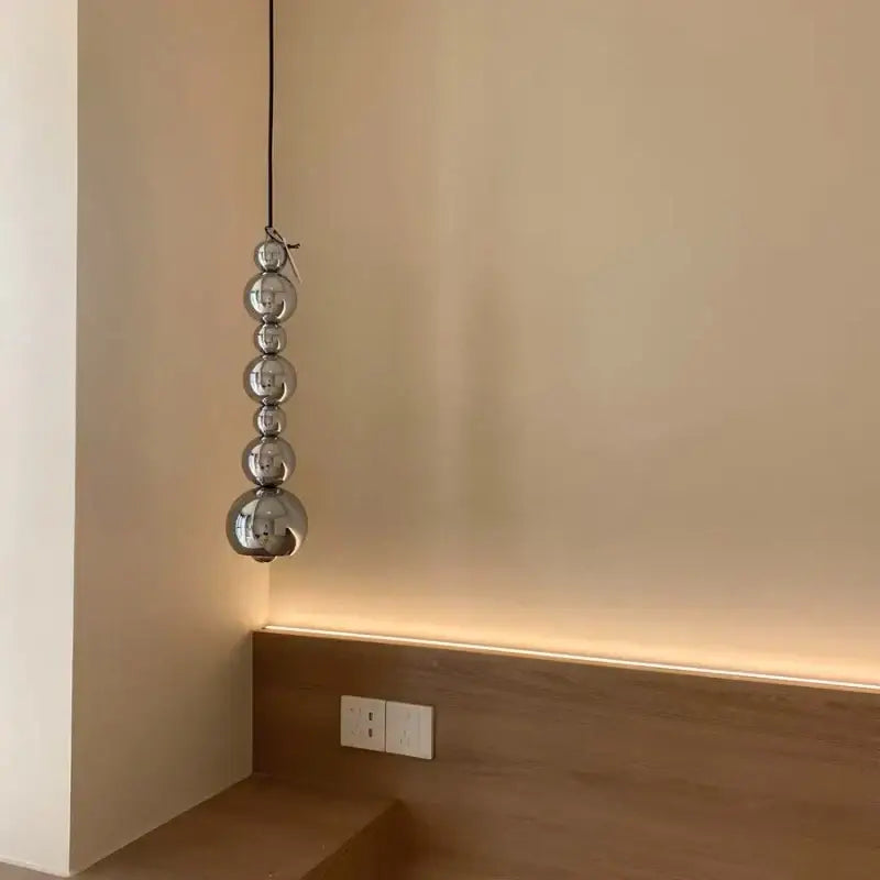 Modern chrome multi ball pendant light source featuring five polished chrome spheres suspended by a black cord