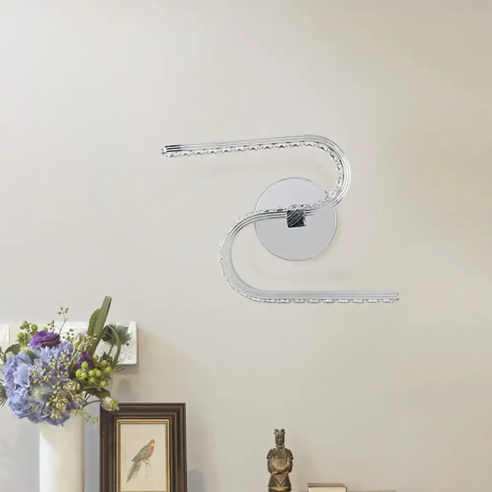 Modern chrome s-shape led wall sconce with acrylic shade and crystal accents emitting warm white light for bedroom use