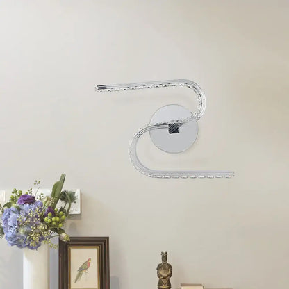 Modern chrome s-shape led wall sconce with acrylic shade and crystal accents emitting warm white light for bedroom use