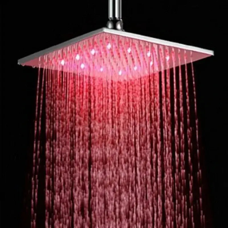 Modern chrome square rain shower head with integrated red led lights illuminating falling water in bathroom fixture