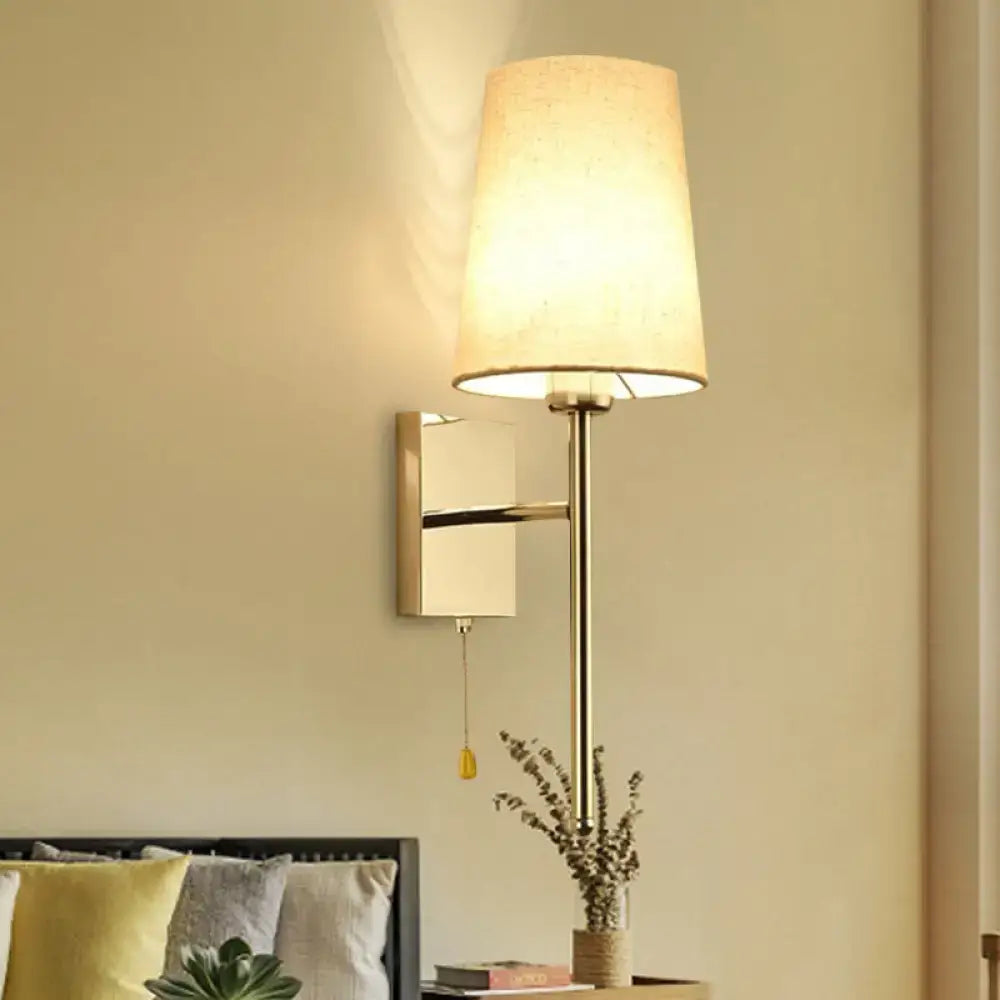 Modern gold-toned tapered wall sconce with a tall slender stem and soft beige fabric shade for bedroom lighting