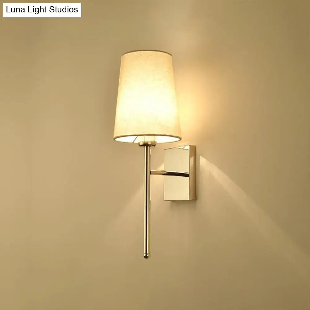 Modern chrome tapered wall sconce with a sleek chrome finish and off-white fabric shade for bedroom lighting