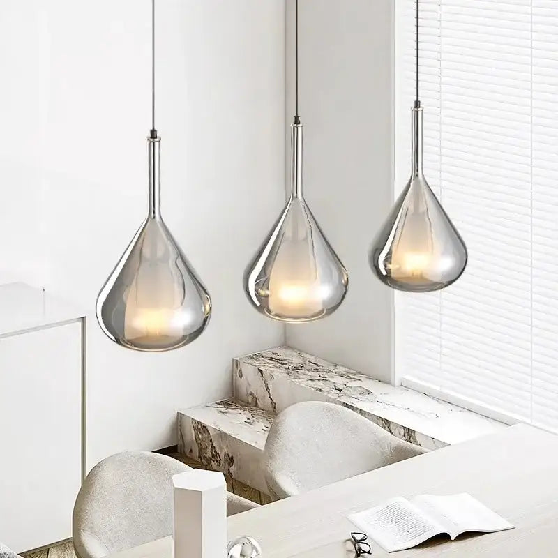 Three sleek chrome chandelier pendant lights with a teardrop shape hang from the ceiling for dining room use