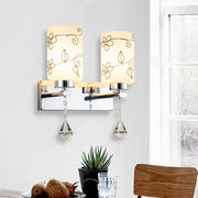 A modern chrome white glass cylinder wall sconce with floral patterns and crystal pendants for bedroom lighting