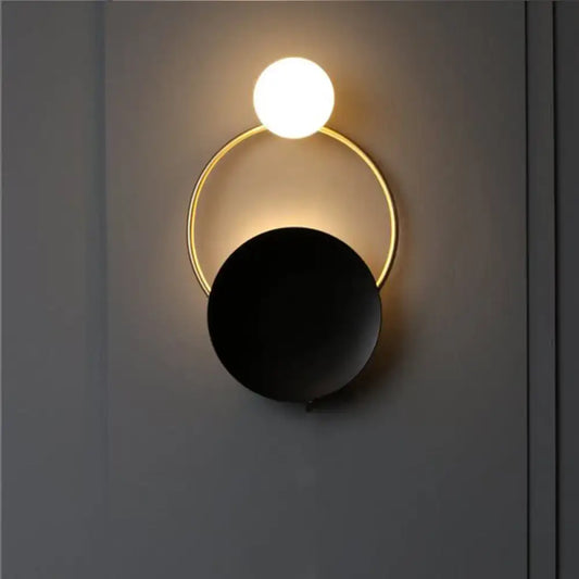 Modern circle wall sconce with a glowing white sphere suspended above a gold ring and matte black disc for bedroom lighting