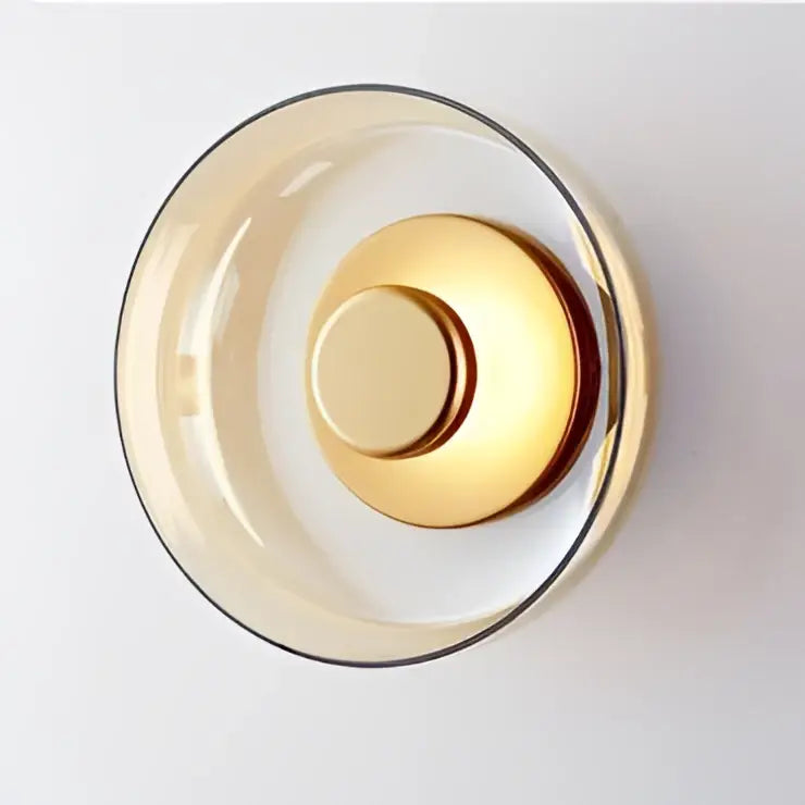 A modern circular glass bowl led wall sconce with a translucent amber glass shade and polished gold-toned base for decorbites