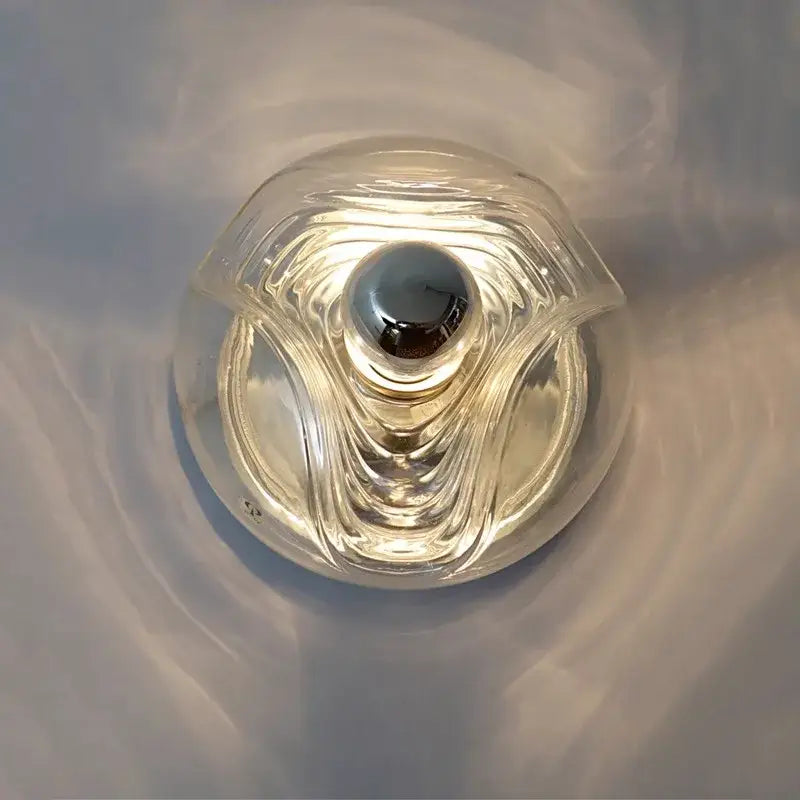 Modern circular swirling clear glass wall lamp with sculpted wave design and polished chrome bulb by decorbites designer glass wall