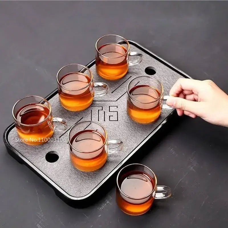 Black textured tea tray with five glass teacups filled with amber liquid in modern 2pc 120ml glass handle coffee set