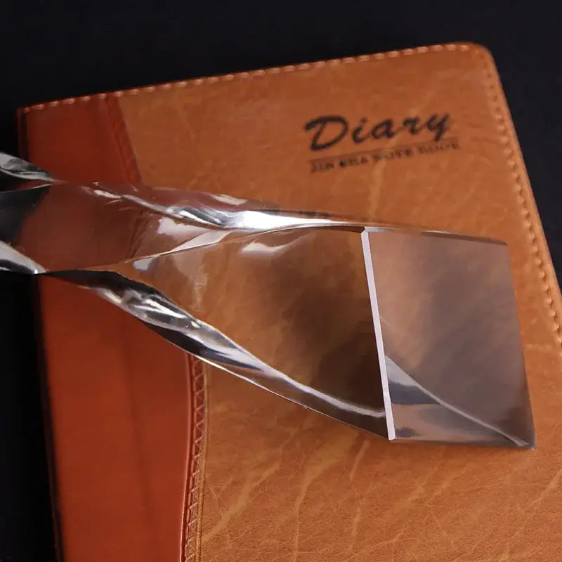 Brown leather diary with embossed text and stitched edges shown alongside a modern clear blue glass twisted column trophy office award