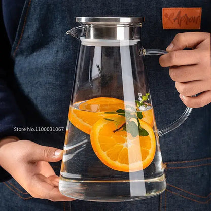 Modern clear borosilicate glass pitcher with stainless steel lid filled with water orange slices and mint leaves