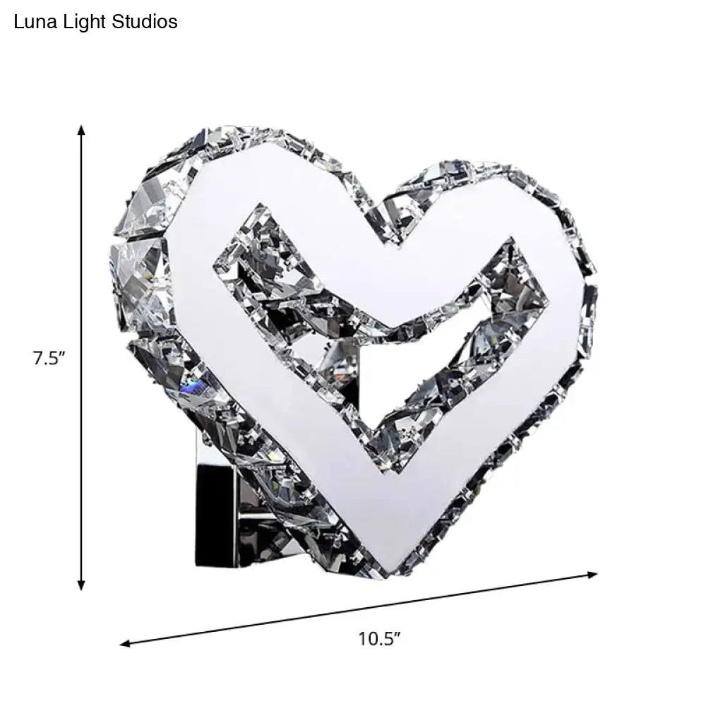 A modern clear crystal heart wall lamp with faceted edges and a mirrored center by luna light studios emitting warm white light