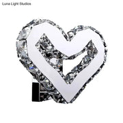 A modern clear crystal heart wall lamp with faceted crystal accents on a chrome base emitting warm white light