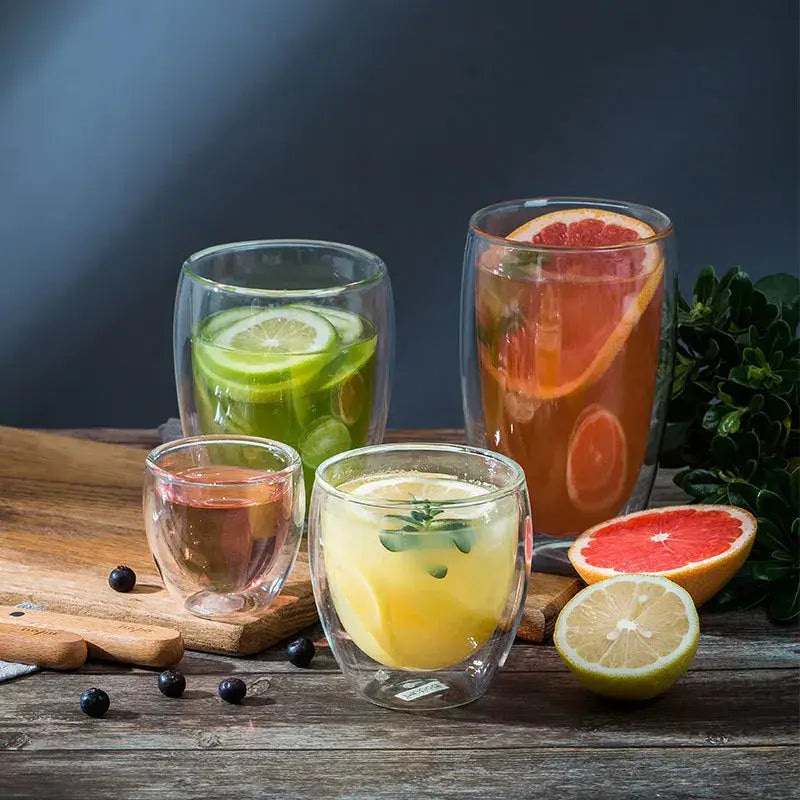 Set of modern clear double wall borosilicate glass tumblers with citrus slices and herbs in colorful beverages
