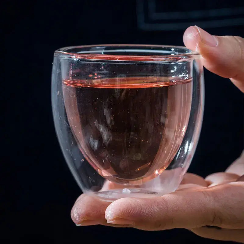 A clear double wall borosilicate glass tumbler filled with rose liquid held gently in hands for modern espresso use