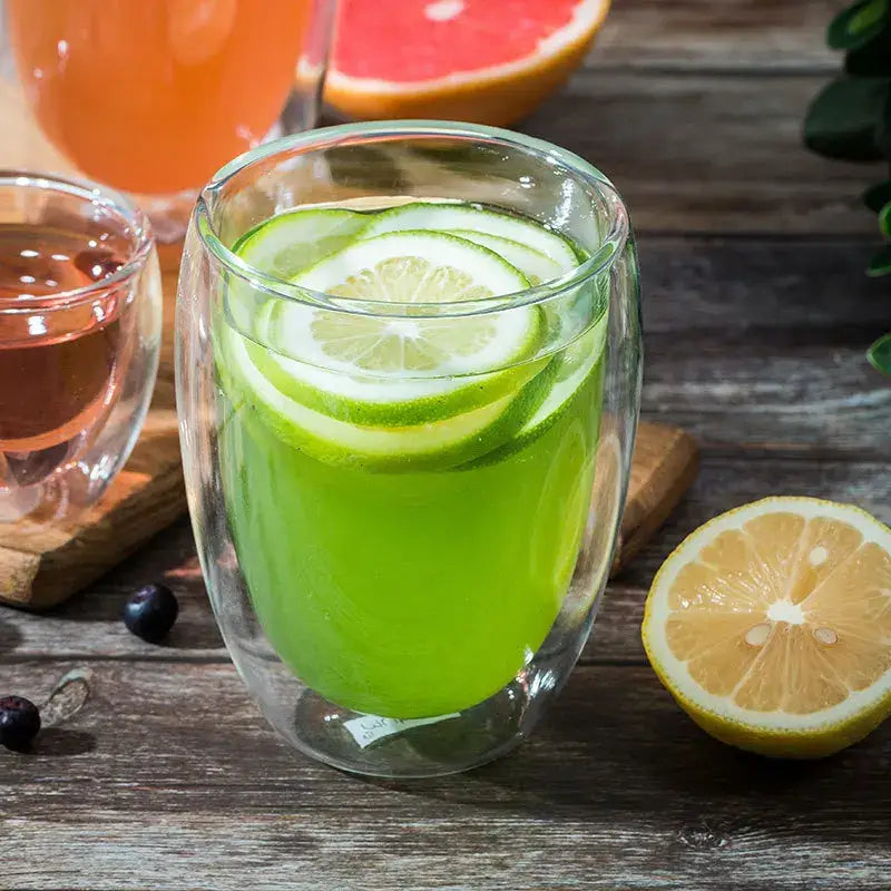 Modern clear double wall borosilicate glass espresso cup filled with citrus drink and lime slices in vibrant green