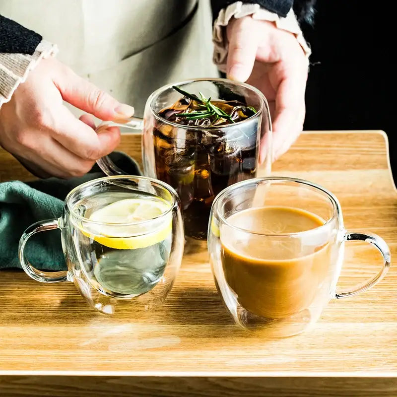 Modern clear double wall glass cup set featuring clear double walled glass mugs with handles filled with beverages