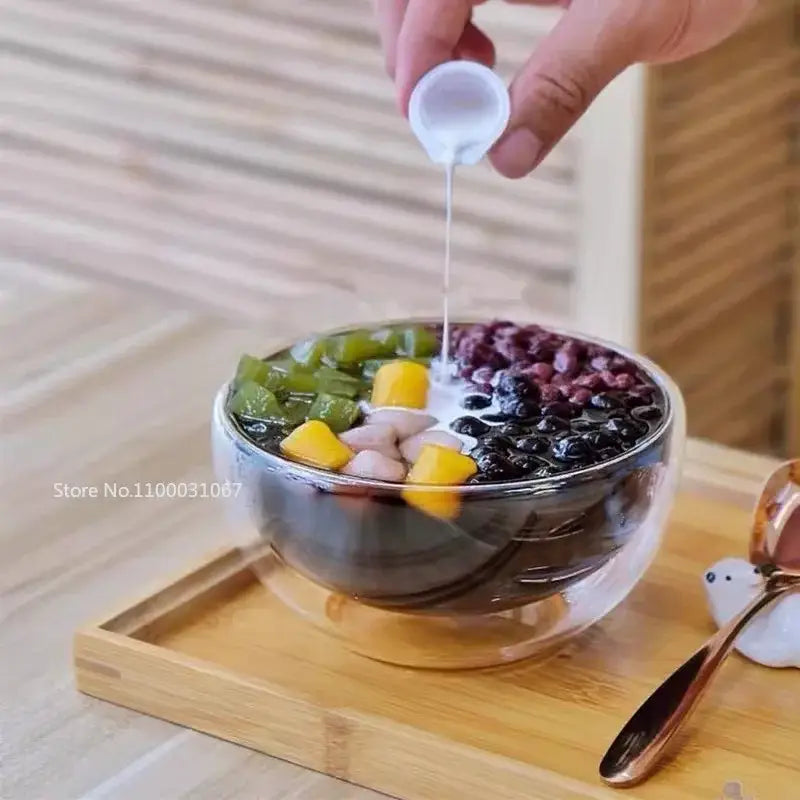 A clear double wall glass salad bowl filled with colorful tapioca pearls mango chunks and purple beans