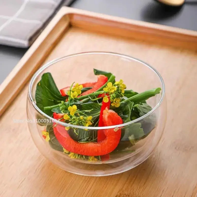Modern clear double wall glass salad bowl filled with red bell pepper slices and green leafy vegetables garnished with yellow flowers