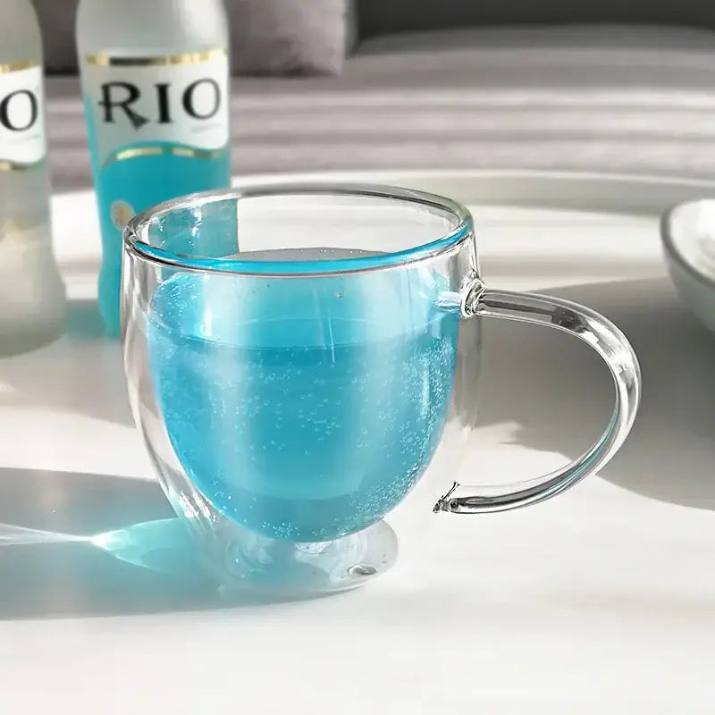A modern clear double wall glass coffee mug with a sleek handle filled with vibrant blue liquid and subtle reflections