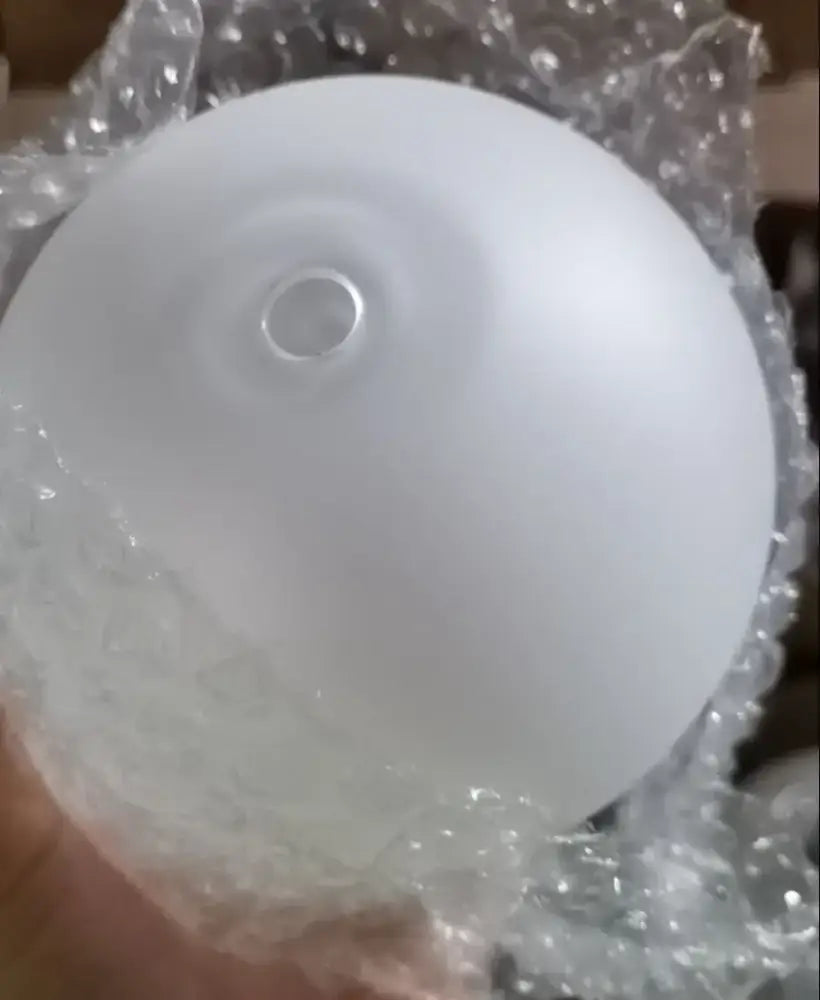 A frosted white glass ball pendant light with a central mounting hole wrapped in bubble wrap for dining room use