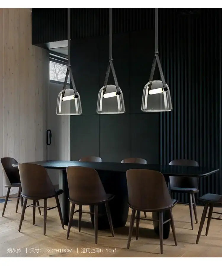 Three modern pendant light fixtures with clear glass shades and black leather straps hang above a dining table