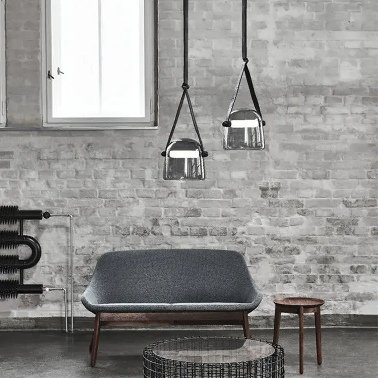 Two modern clear glass pendant light fixtures with black leather straps hang from the kitchen ceiling