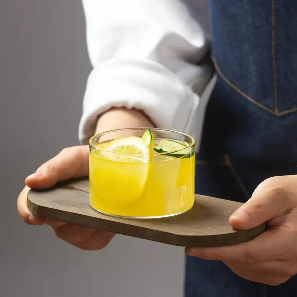 Modern clear glass cup set featuring a decorbites glass cup with vibrant yellow liquid garnished with lemon and cucumber