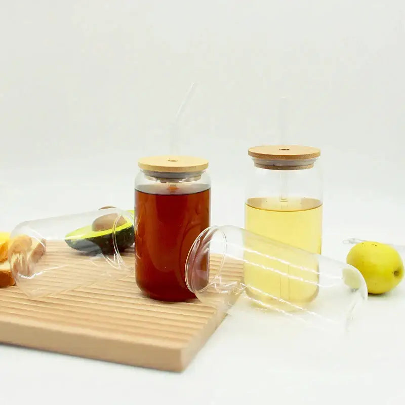 Two decorbites glass cups made of clear glass with bamboo lids and straws filled with amber and yellow drinks