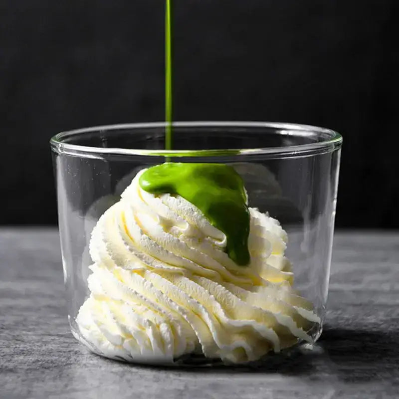 A clear glass dessert cup filled with whipped cream topped with vibrant green matcha sauce from a dessert cup set