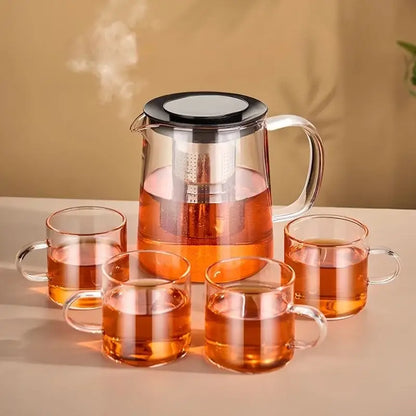 Modern clear glass flower teapot with borosilicate glass infuser pitcher and four mugs filled with amber tea