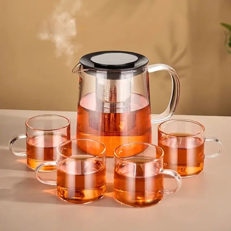 Modern clear glass flower teapot with borosilicate glass infuser pitcher and four mugs filled with amber tea