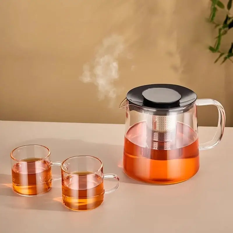 Modern clear glass flower teapot with black lid and stainless steel infuser filled with steaming amber tea