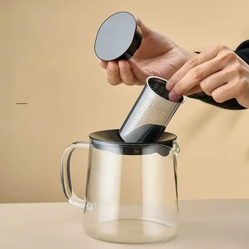 Black and silver stainless steel tea infuser being inserted into a clear borosilicate glass flower teapot with matching lid