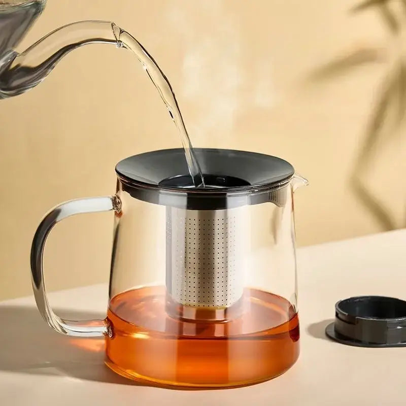 Modern clear glass flower teapot with stainless steel infuser filled with amber tea made of borosilicate glass