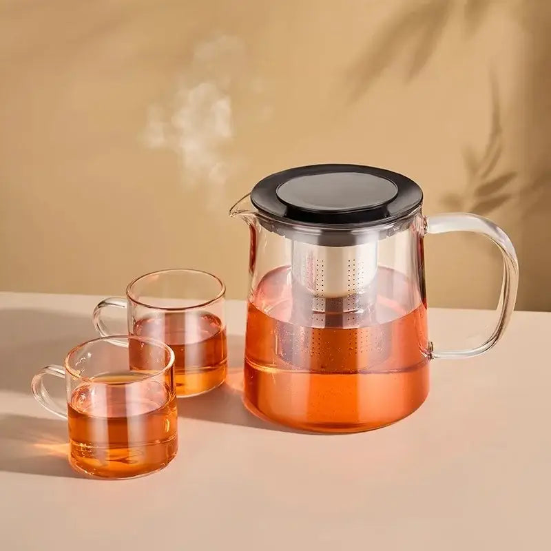 Modern clear glass flower teapot with black lid and white infuser filled with amber tea for kitchen use