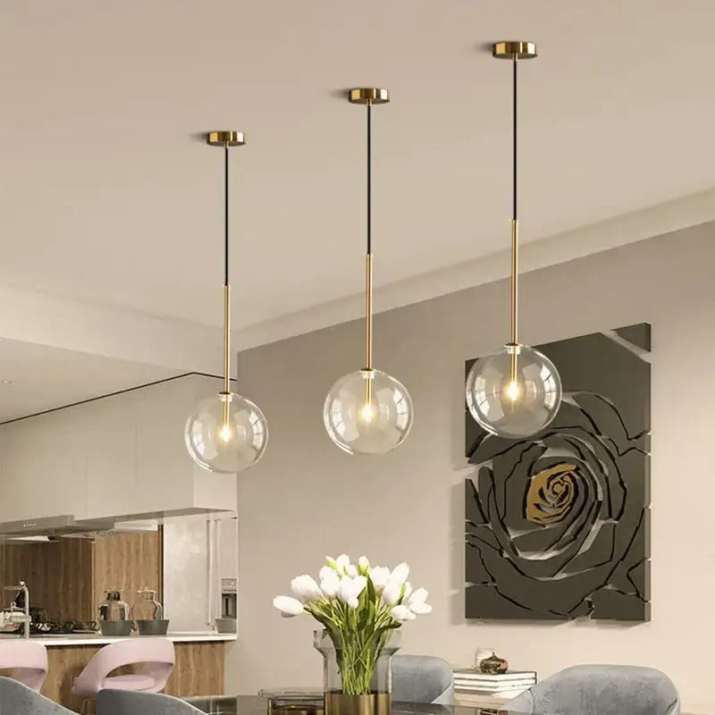 Three modern pendant lights with clear glass globe shades and brass fixtures hanging from black cords for kitchen rod suspension