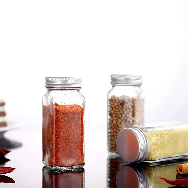 Modern clear glass seasoning jar set with silver lids containing red powder white peppercorns and yellow granules