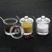Modern clear glass seasoning jars with lids and metal spoons containing various spices in a spice jar set