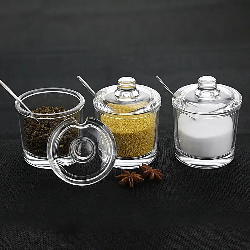 Modern clear glass seasoning jars with lids and metal spoons containing various spices in a spice jar set