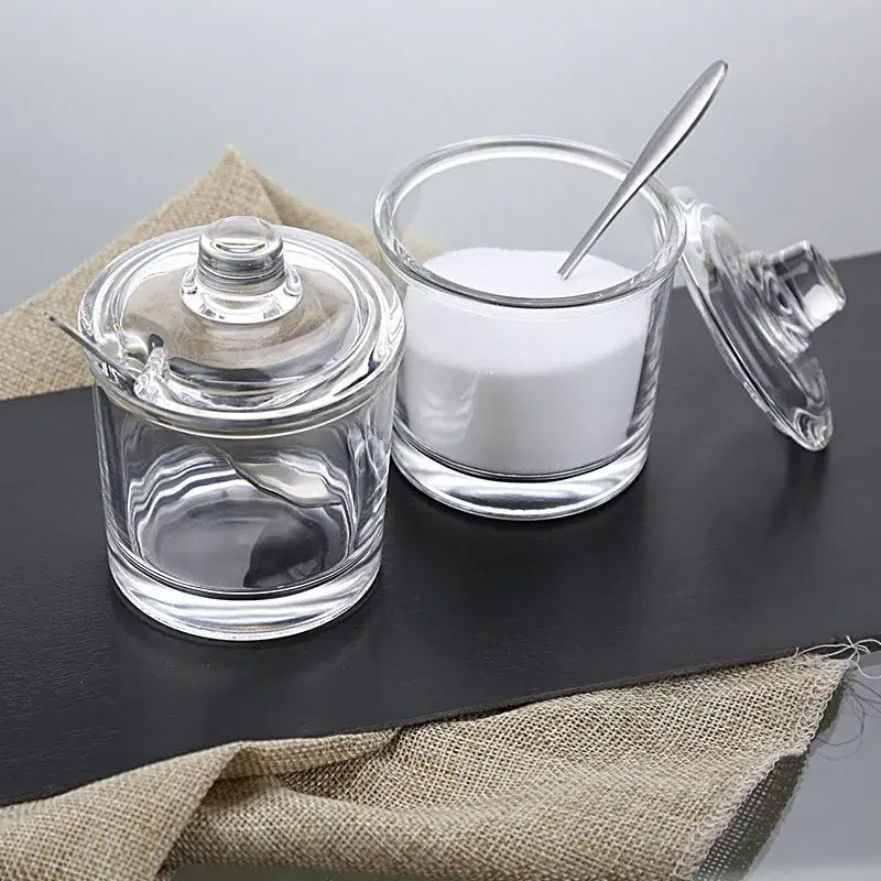 Modern clear glass seasoning spice jar set featuring one filled sugar jar and one empty jar with matching lids