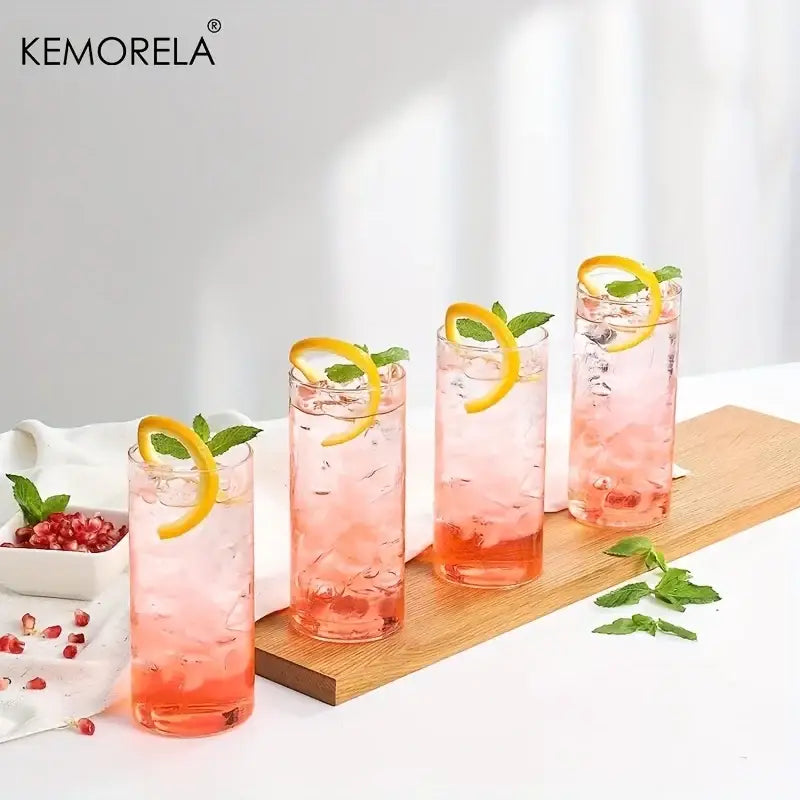 Four modern clear glass tumbler cups filled with pink pomegranate drinks garnished with lemon twists and mint leaves