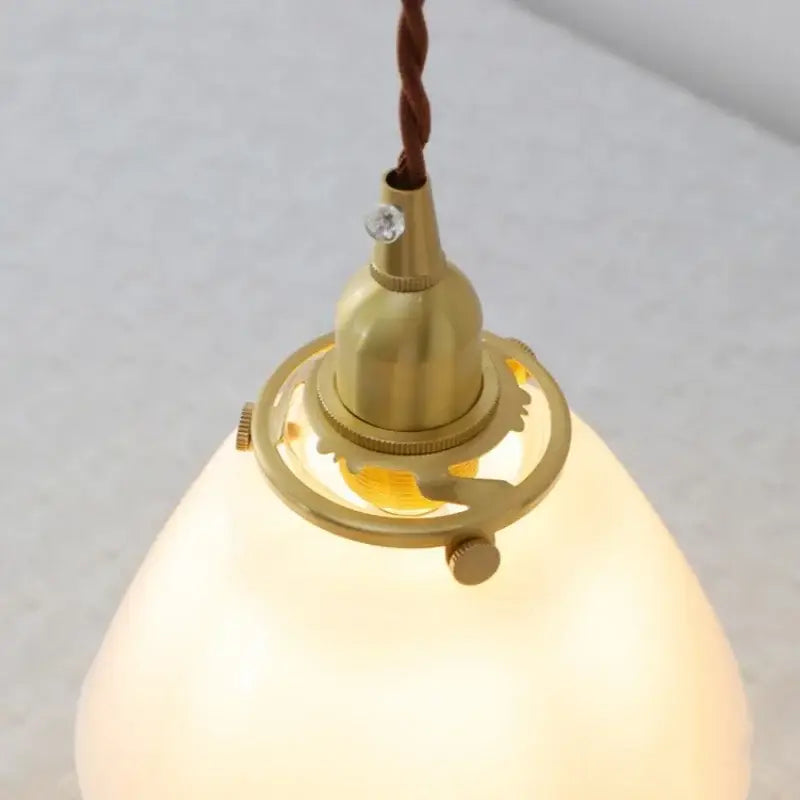 A warm glowing glass led pendant lamp with brass finish and off-white shade ideal for modern kitchen lighting
