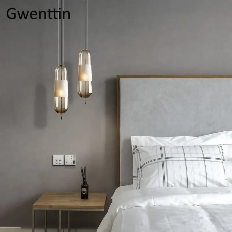 Gwenttin modern pendant lights with clear and smoked cylindrical glass pendant shades and metallic frames above bed