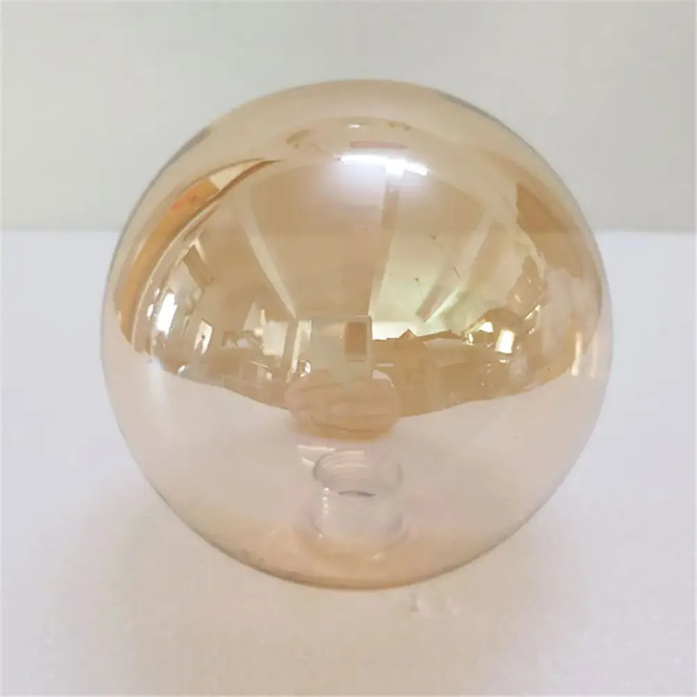 A translucent amber glass sphere glass shade replacement with smooth reflective surface on a small clear base