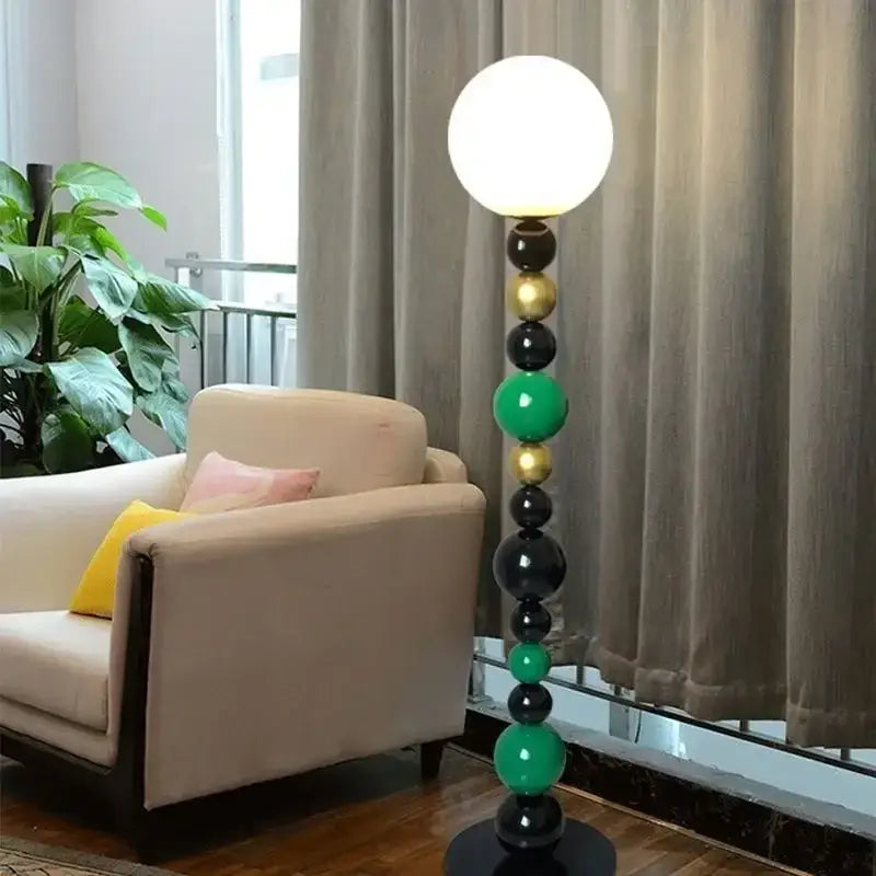 A modern floor lamp with a spherical white glass shade and a colorful glass ball base in black green and gold