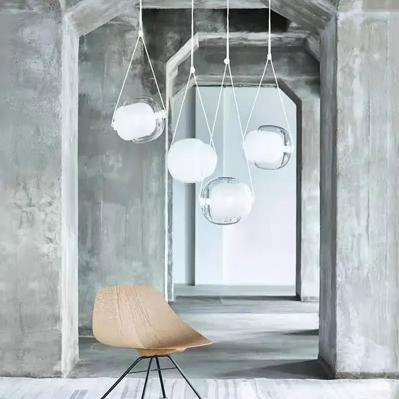 Modern minimalist pendant light with clear colorful glass capsule and white fabric cords hanging in concrete archway