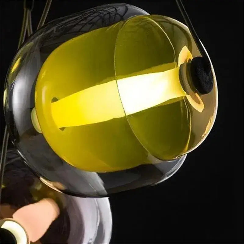 A modern colorful glass capsule led pendant light with a translucent yellow shade and dark reflective casing for kitchen bar
