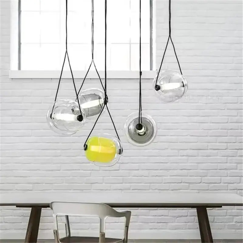 Modern colorful glass capsule led pendant light with clear glass spheres black cords and a yellow interior for kitchen bar